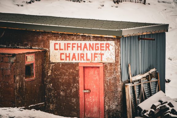 Weathered building with a sign reading "Cliffhanger Chairlift" in a snowy landscape.