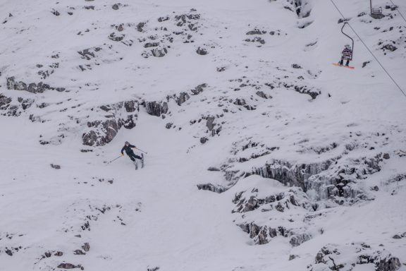 Skiers navigating a snowy slope with a ski lift in the background.